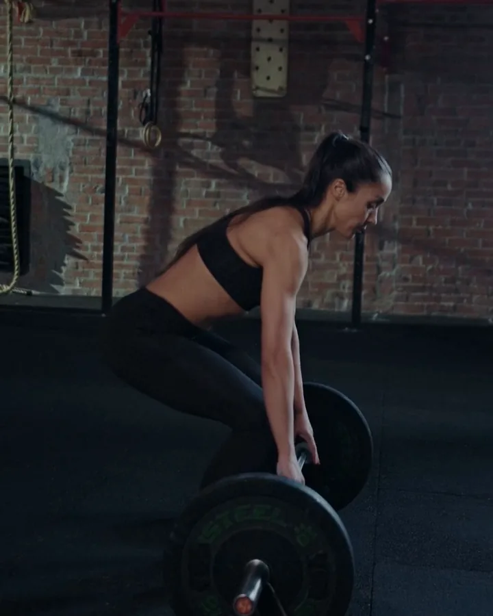 A woman in the middle of a deadlift, seen from the side, hips back and back flat