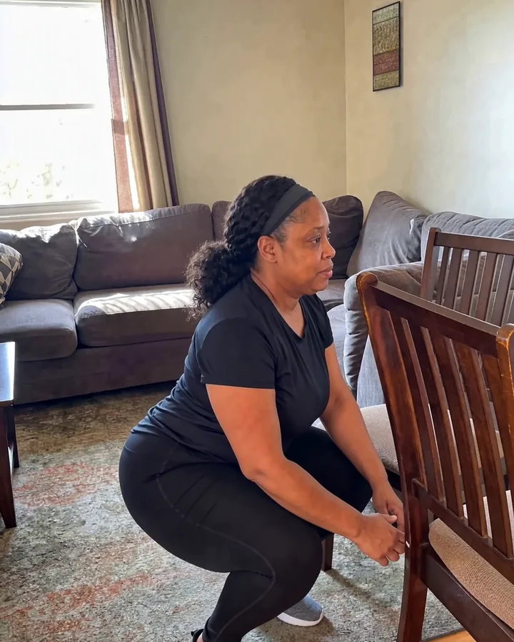 The same woman at the bottom of a squat to a chair, still fully in frame