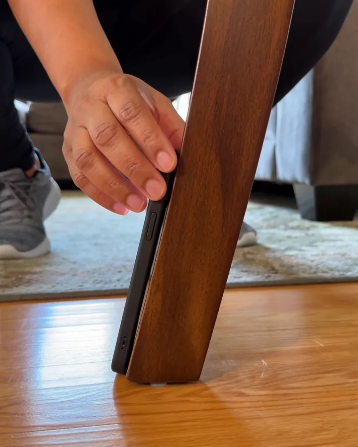 A phone propped upright against the leg of a wooden dining chair on a living-room floor